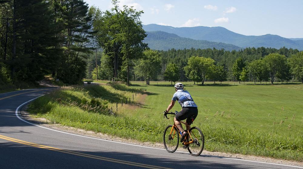 A man rounds a turn on a bike along a green valley.