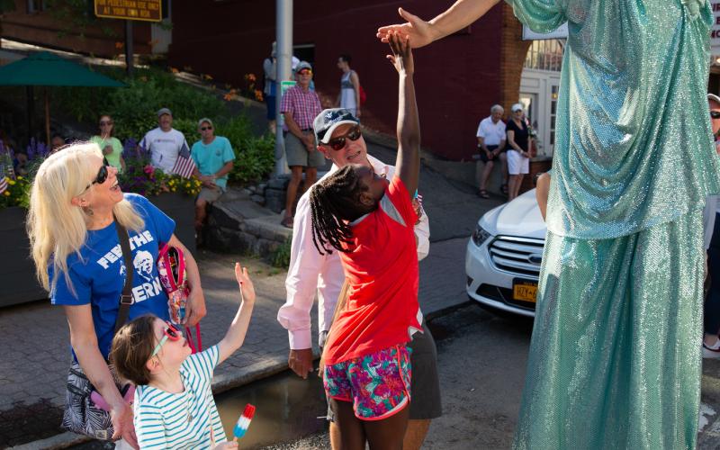 Girl reaches up the give a high five to a women dressed as the Statue of Liberty in the Lake Placid July 4th Parade