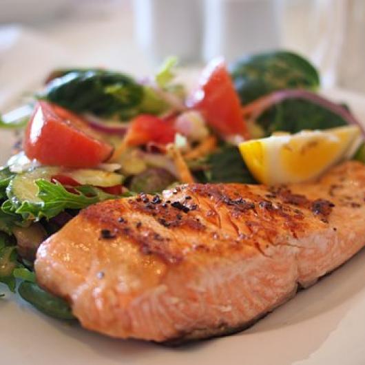 A plate of a cooked salmon fillet with vegetables on the side.