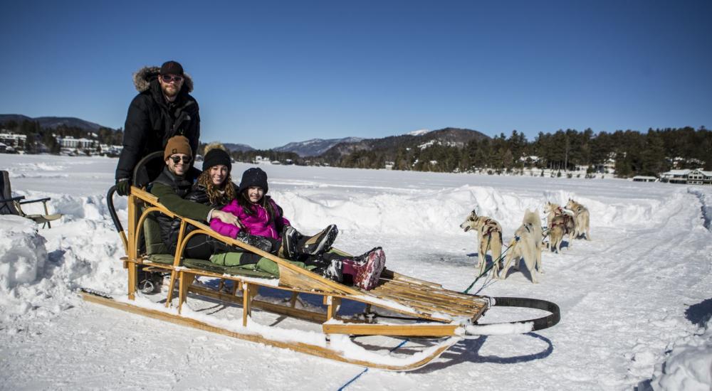 A family of three sits in a dog sled on snowy, frozen Mirror Lake.