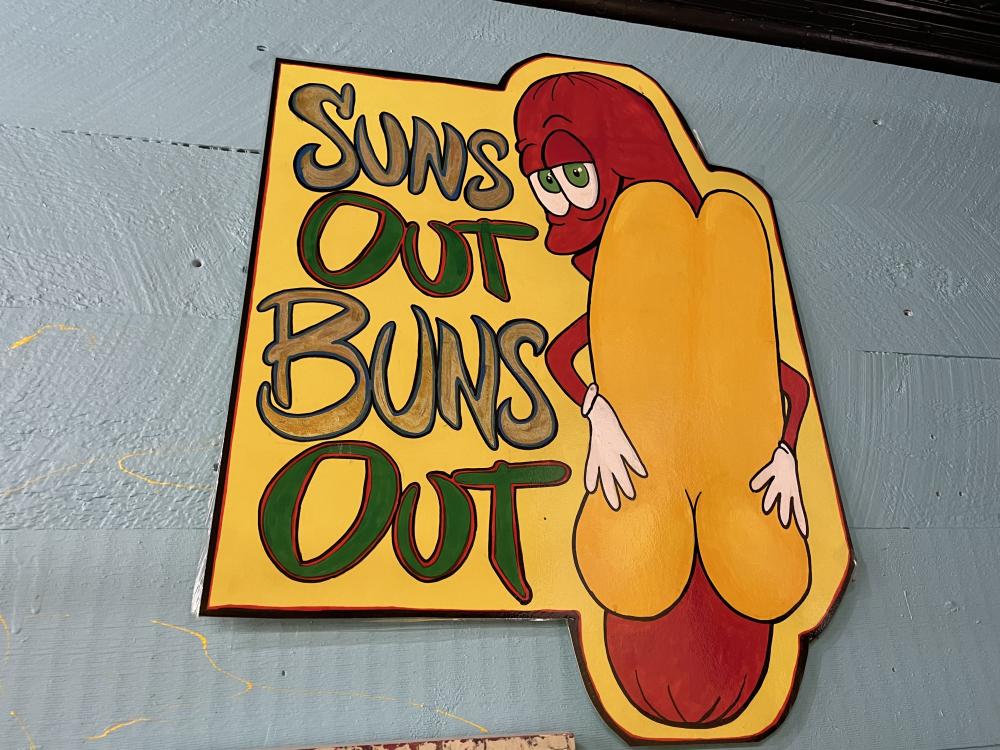 A vivid sign of a hot dog reads, "Sun's out, buns out!"
