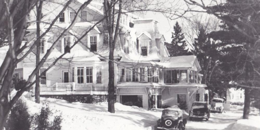 Vintage black and white photograph of the original Mirror Lake Inn, with early automobiles parked on the drive. Image courtesy Mirror Lake Inn.