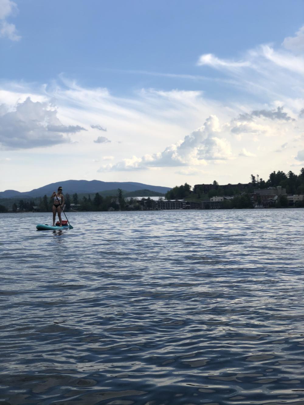 A woman paddles a SUP on a lake with mountains and trees in the background.