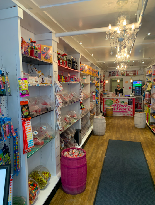 A white shop with chandeliers and shelves filled with brightly colored candy.