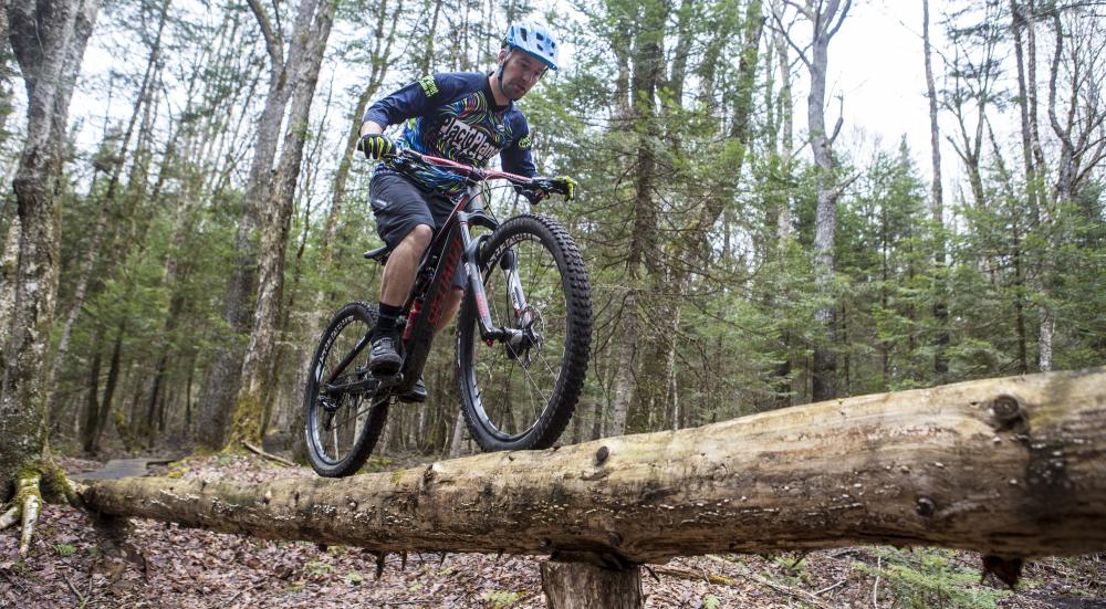 A mountain biker riding on a log in a forest.