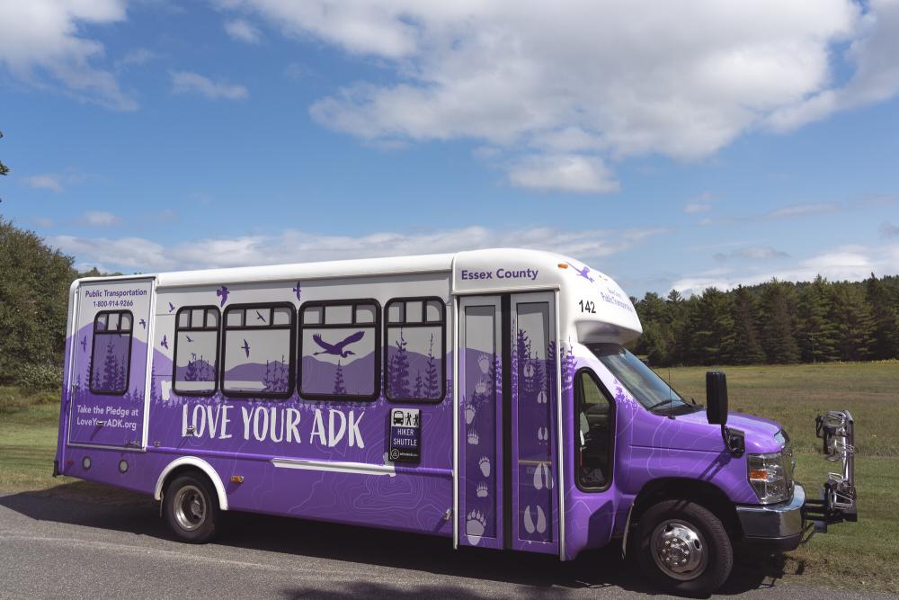A side view of the purple, ADK-themed hiking shuttle bus.