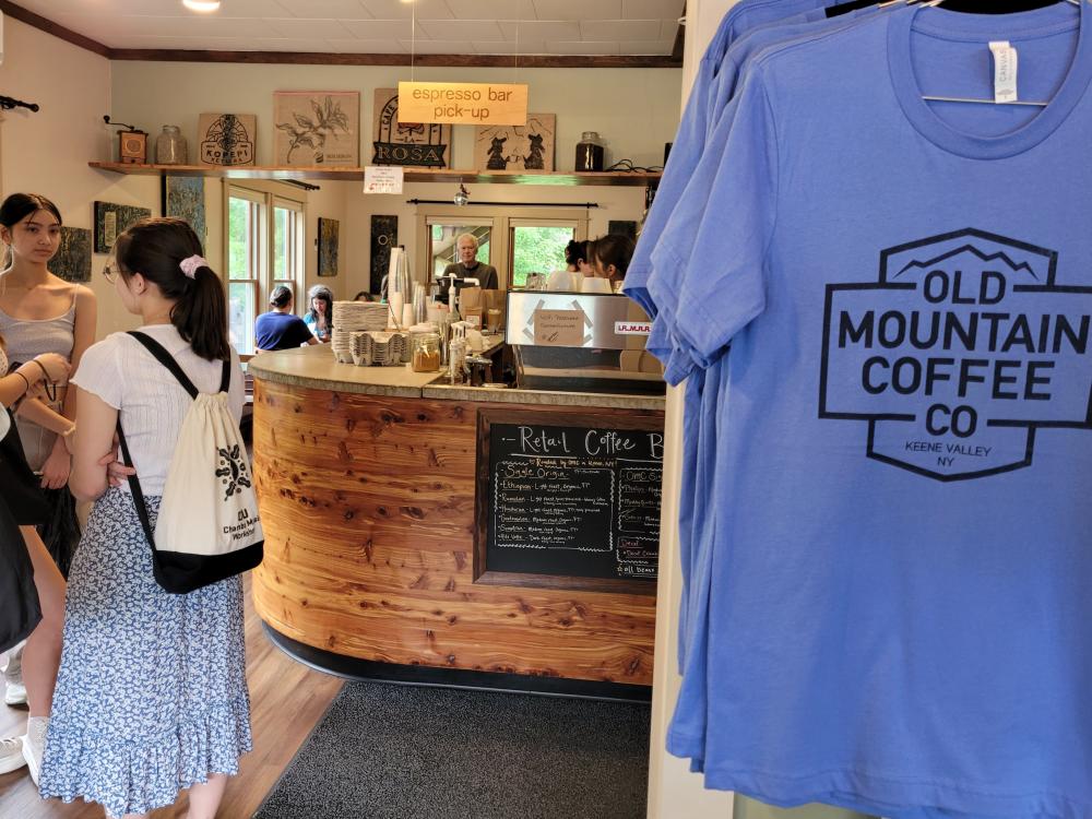 The interior of Old Mountain Coffee with a pastry case, people in line and a blue t-shirt with the company logo