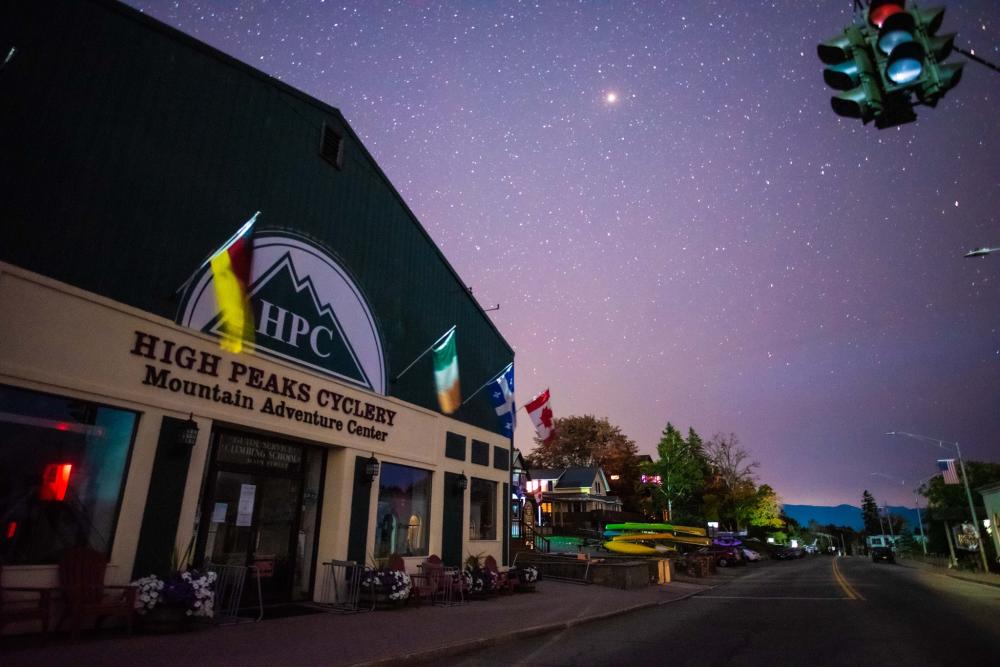 The storefront of High Peaks Cyclery Mountain Adventure Center at night, with a clear shy and bright stars in the sky