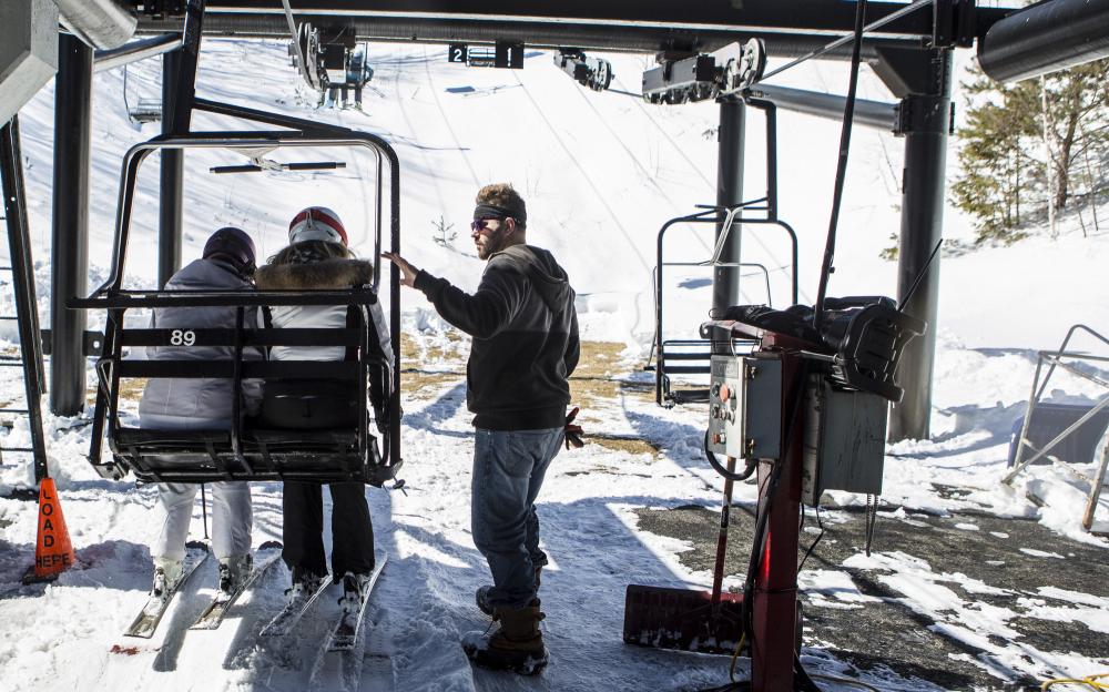 A liftie helps people onto a chairlift.