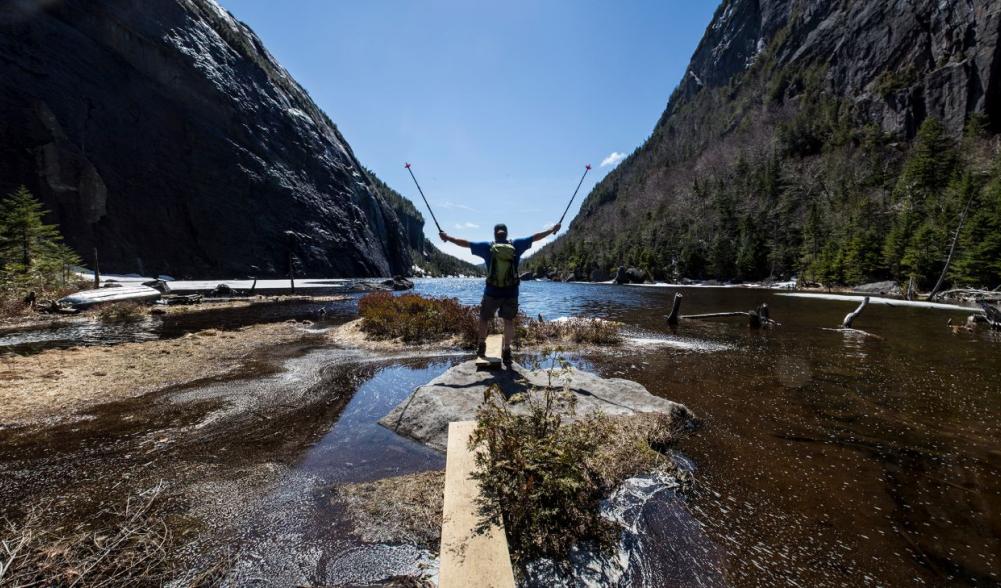 A man posing on the shore of Avalanche Lake while spring hiking in the Adirondacks.