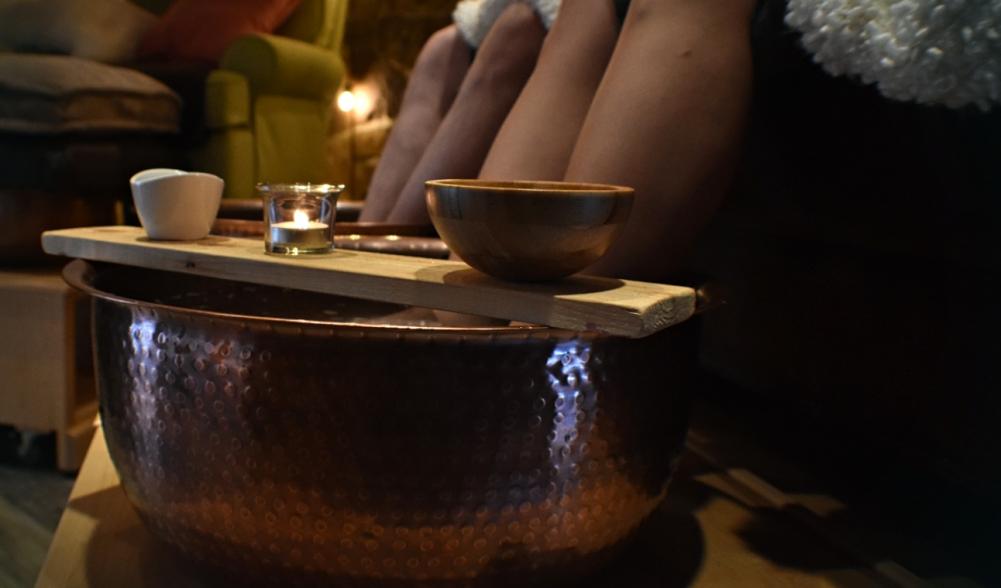 Two people sit with their feet in hammered copper bowls for a foot treatment.