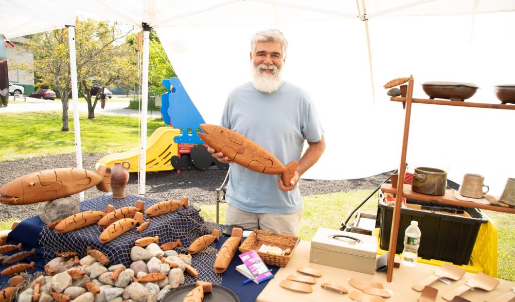 A local craftsman holds up a wooden fish at the farmers market.