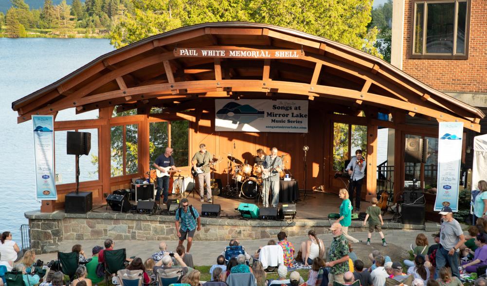A band of four men plays in the bandshell next to Mirror Lake with an audience.