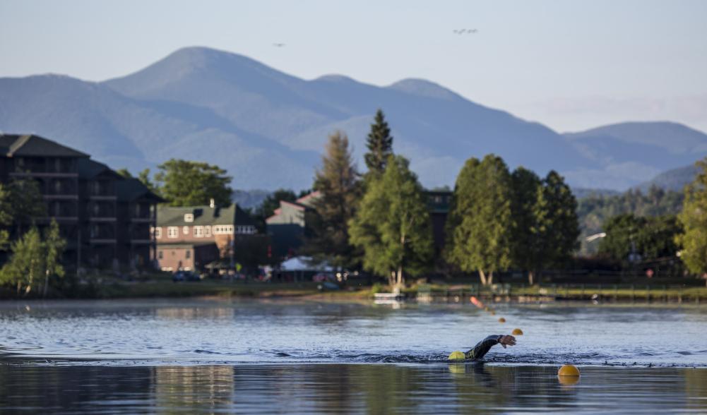 A person swimming in the lake with mountains in the background.