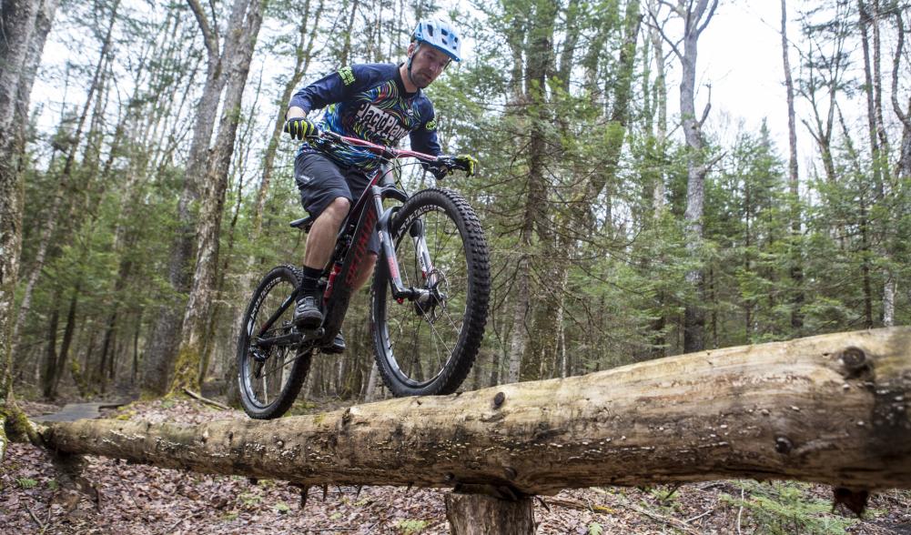 A mountain biker riding on a log in a forest.