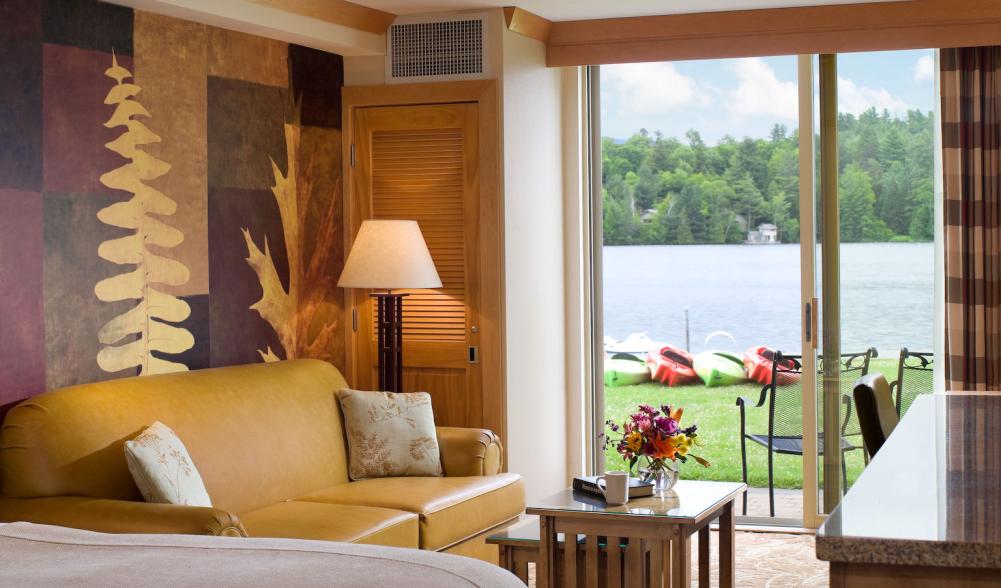 A hotel room with sliding doors opening onto a lakefront lawn with kayaks.