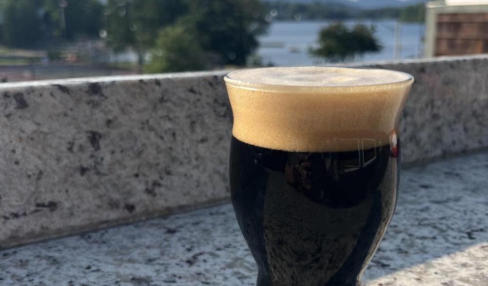 A dark glass of beer with a thick head of foam sits on a stone outdoor bar.