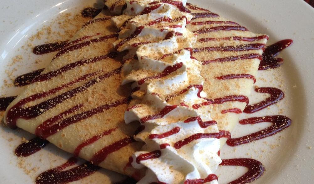A crepe with whipped cream and strawberry jam striped on top.