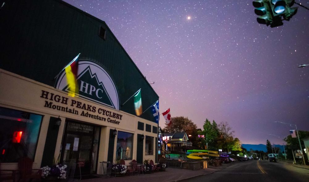 The storefront of High Peaks Cyclery Mountain Adventure Center at night, with a clear shy and bright stars in the sky