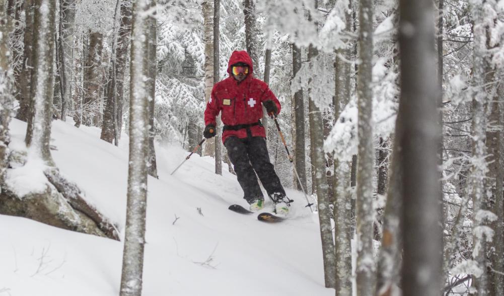 Ski patroller in a red coat skiing through the trees