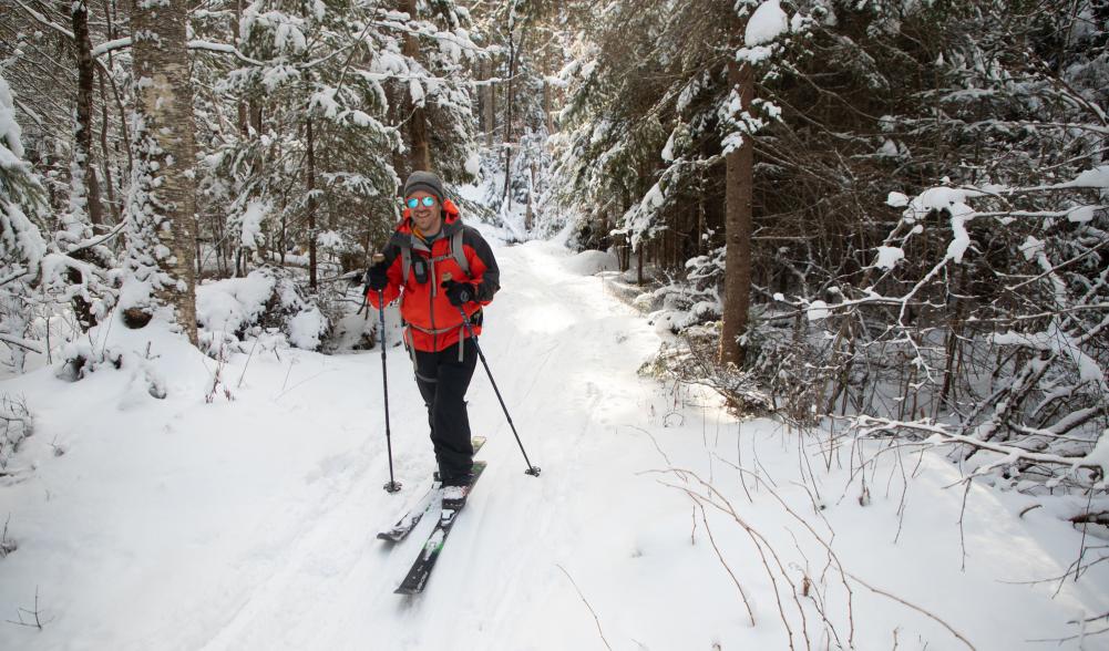 A man smiles as he cross-country skis through a snowy trail.