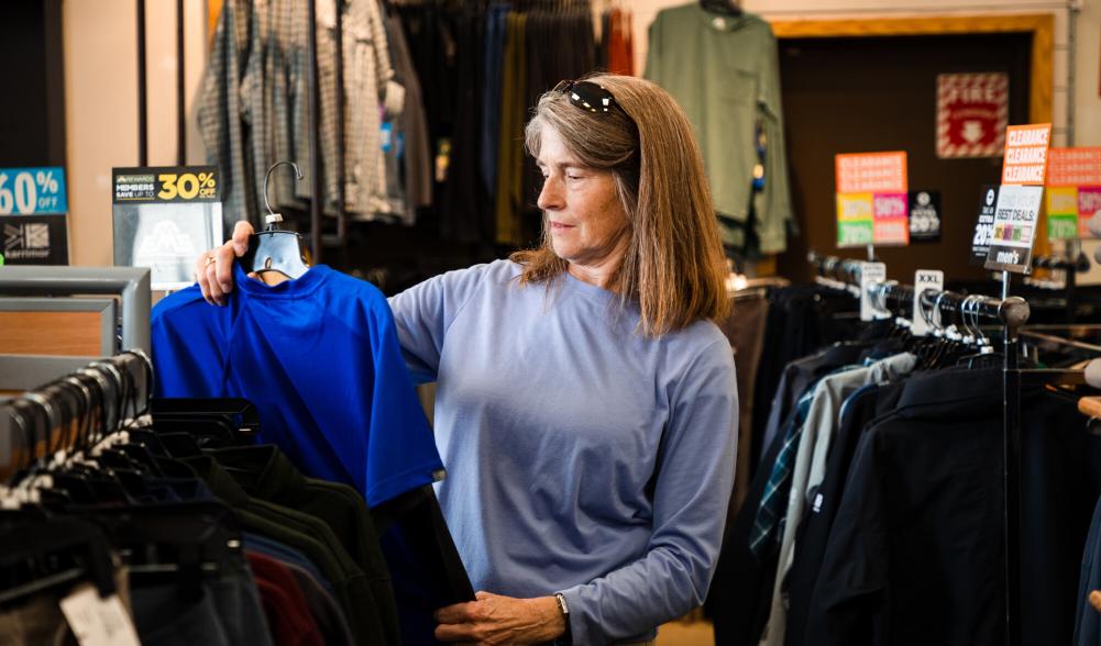A woman contemplates buying a blue t shirt in a store.