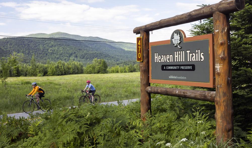 Two people on bikes ride past the Heaven Hill Trails sign.