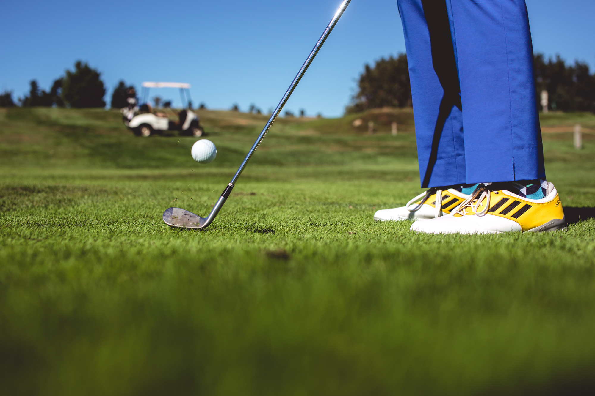 Close-up of a golfer's feet as he strikes the ball with cart in background.