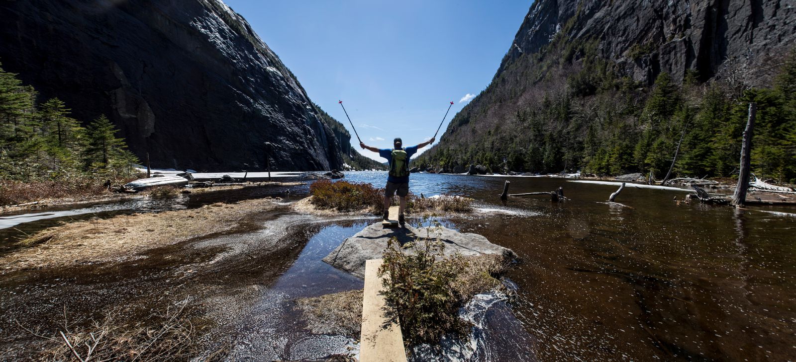 A man posing on the shore of Avalanche Lake while spring hiking in the Adirondacks.