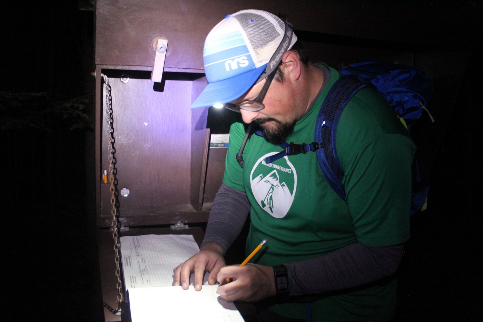 Dan signs the trail register by the light of his headlamp.