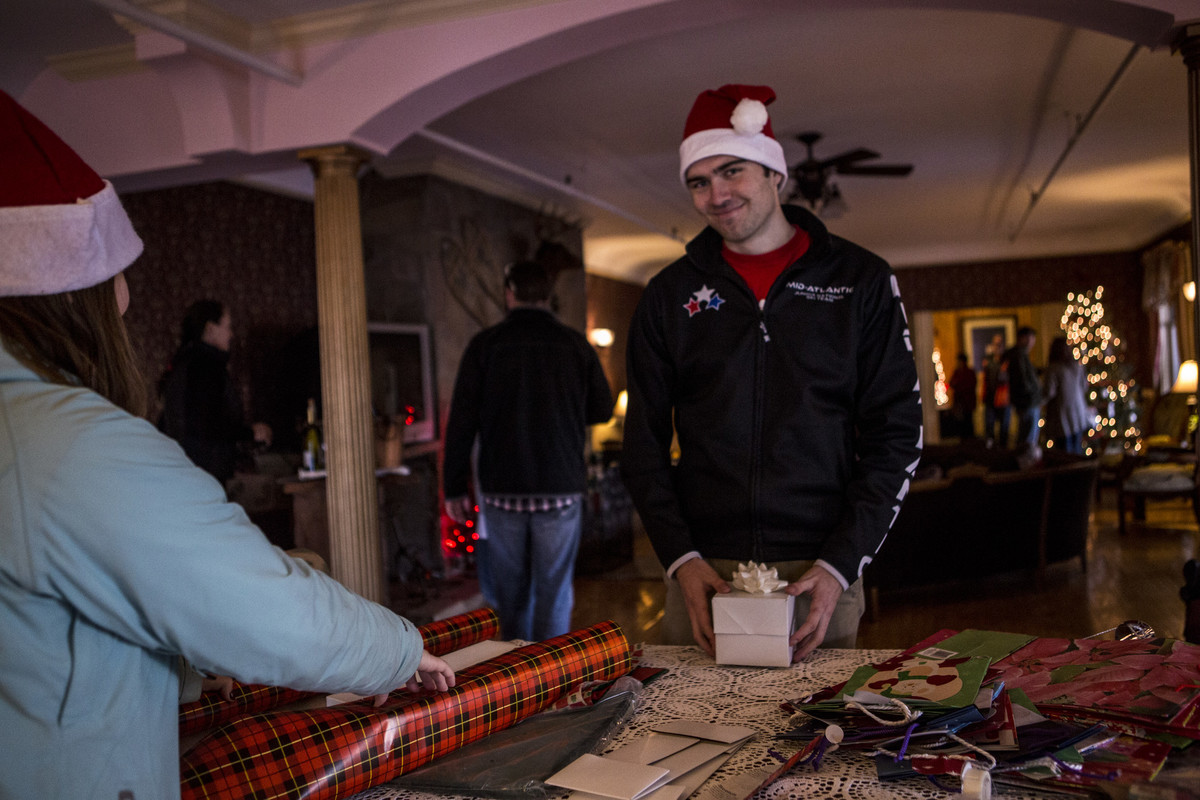 A man in a Santa hat poses at a gift wrapping table.