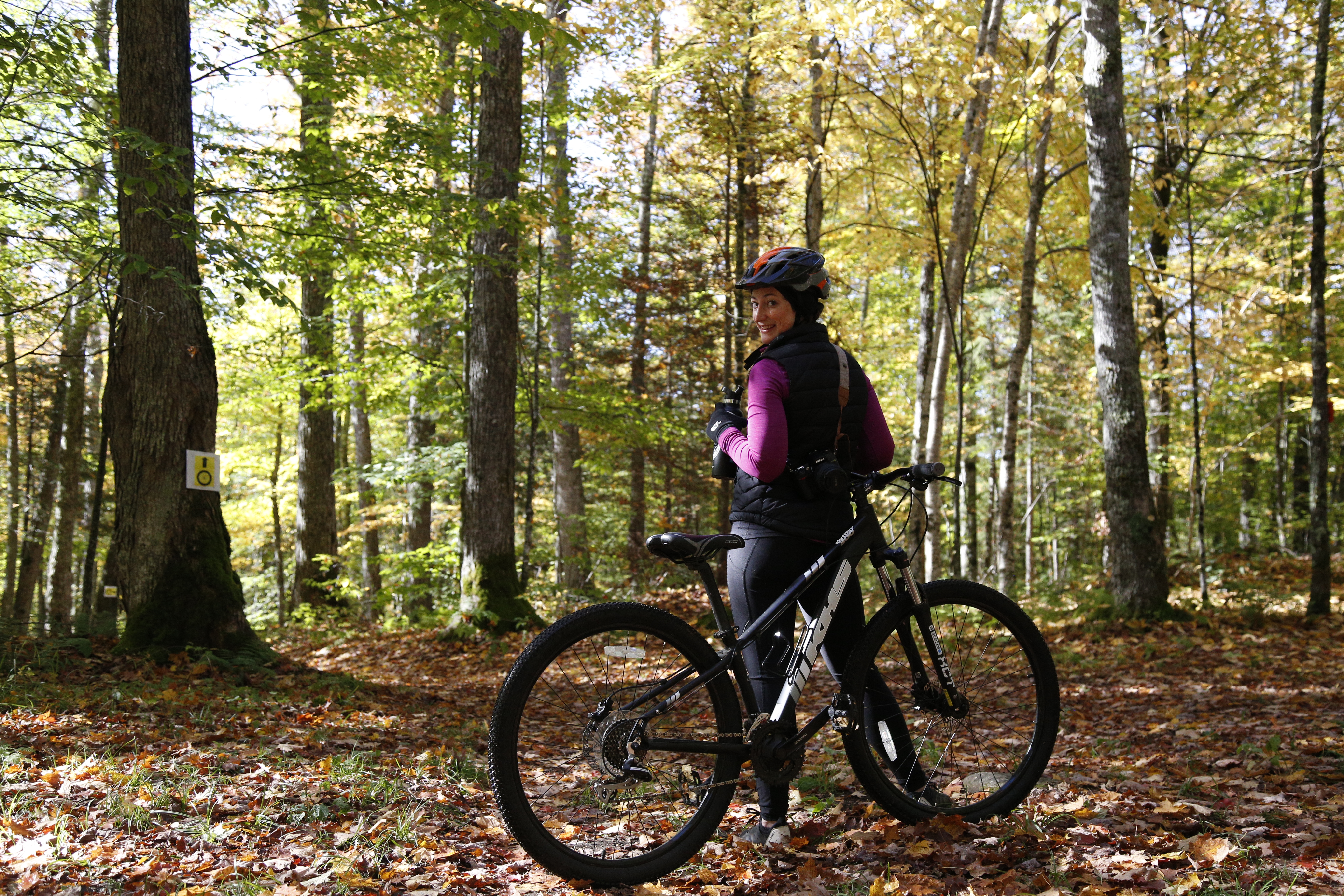 &quot;Female smiling at the camera with a Lake Placid mountain bike rental surrounded by fallen leaves