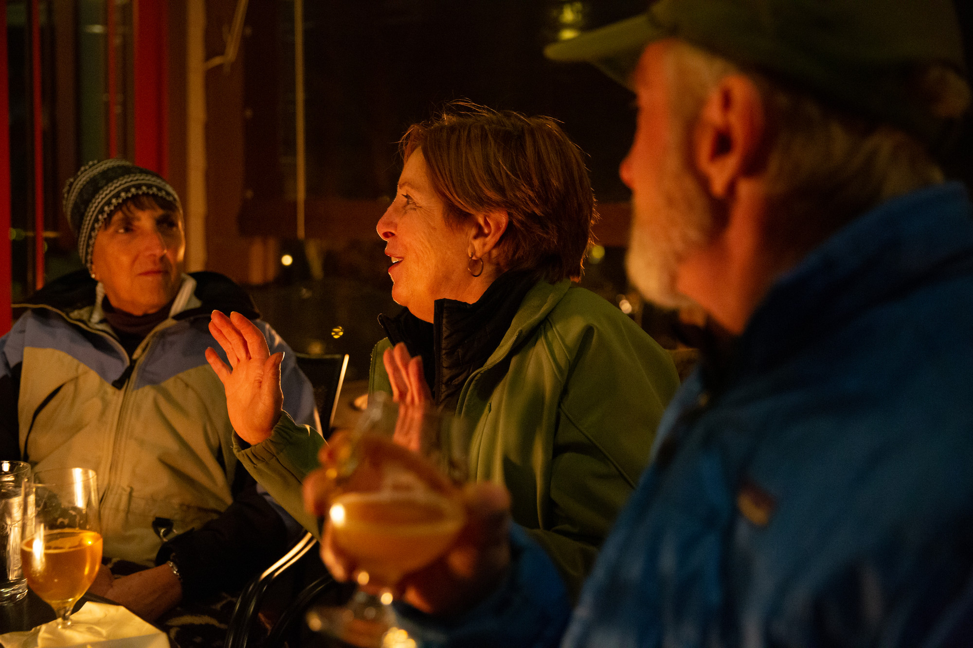 Two women and a man chat over a meal at an outdoor fire in winter.