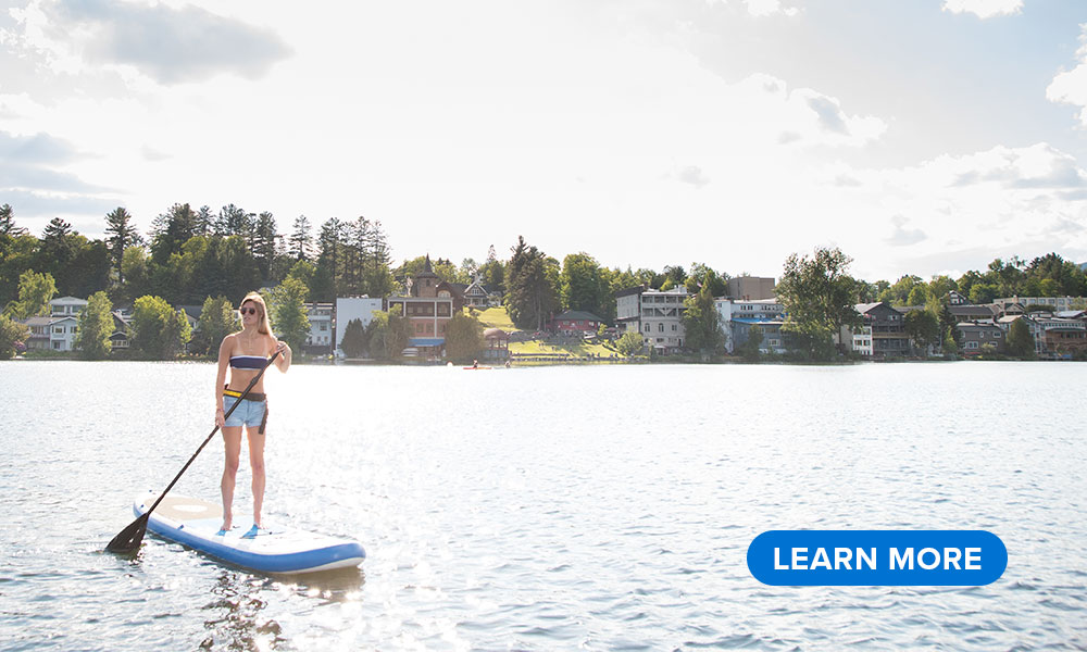 A woman paddles a SUP on Mirror Lake with Main Street in the background.