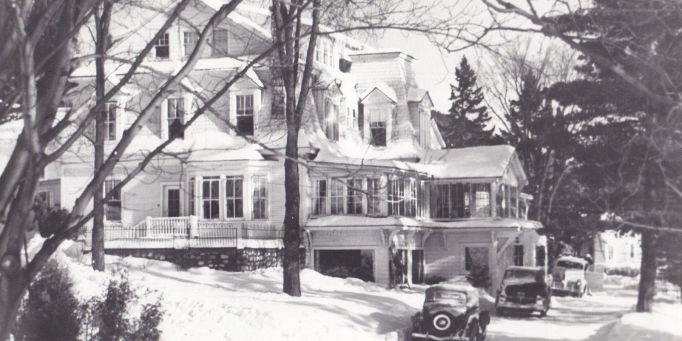 Vintage black and white photograph of the original Mirror Lake Inn&#44; with early automobiles parked on the drive. Image courtesy Mirror Lake Inn.