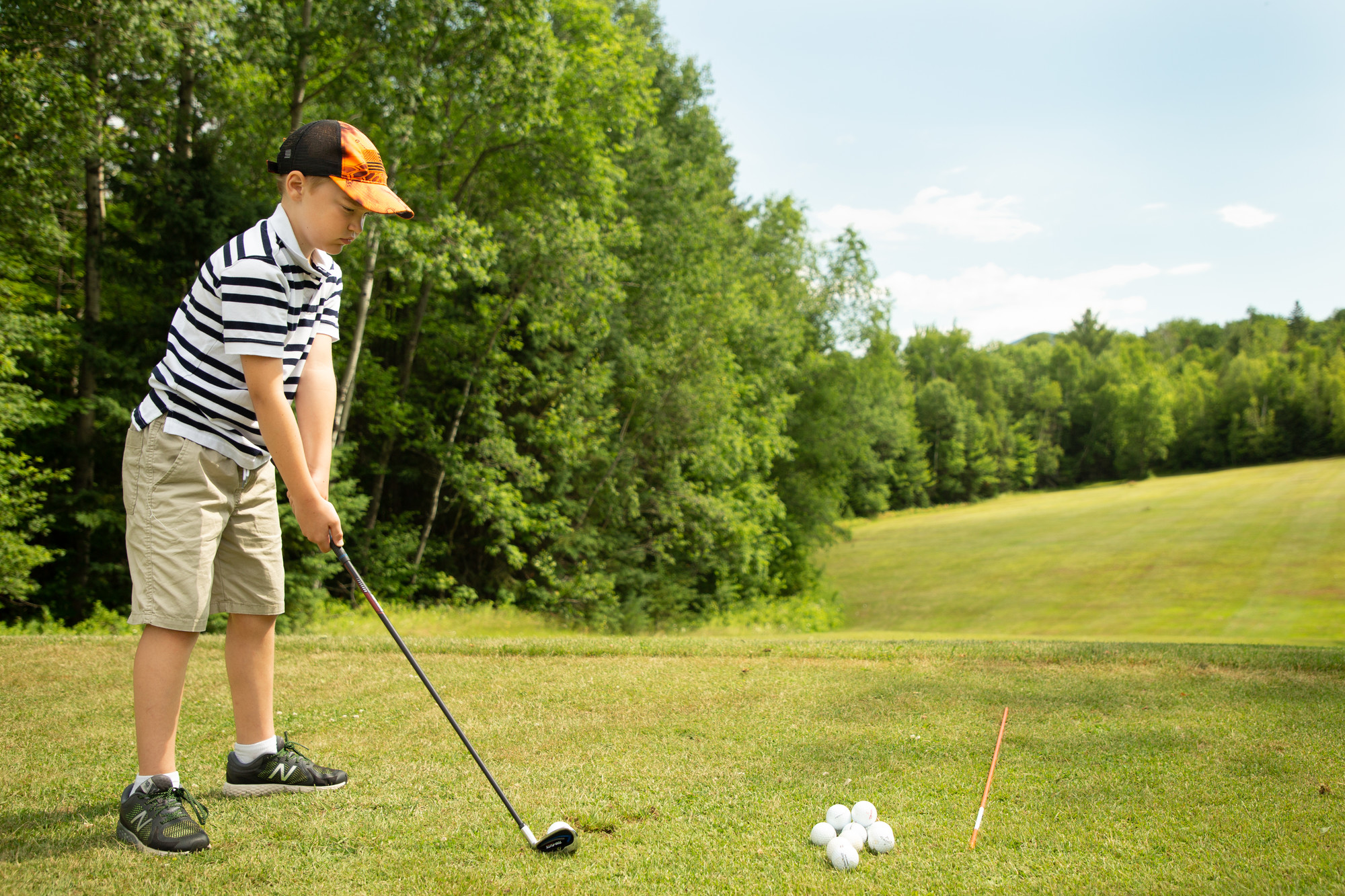 A young boy prepares to tee off on a golf green&#44; with bright green trees along the fairway.