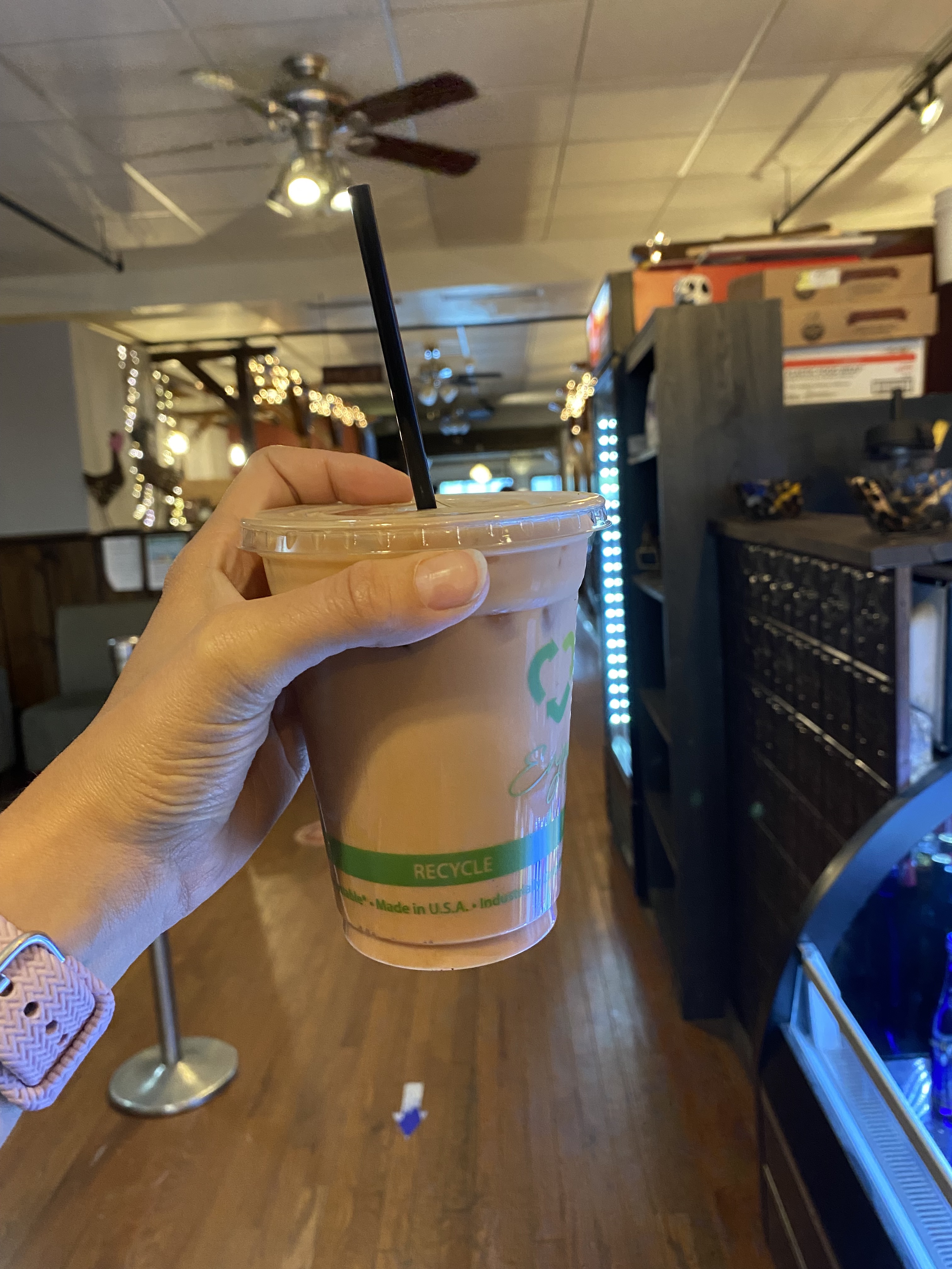A womans hand holds up an iced coffee drink in a shop.