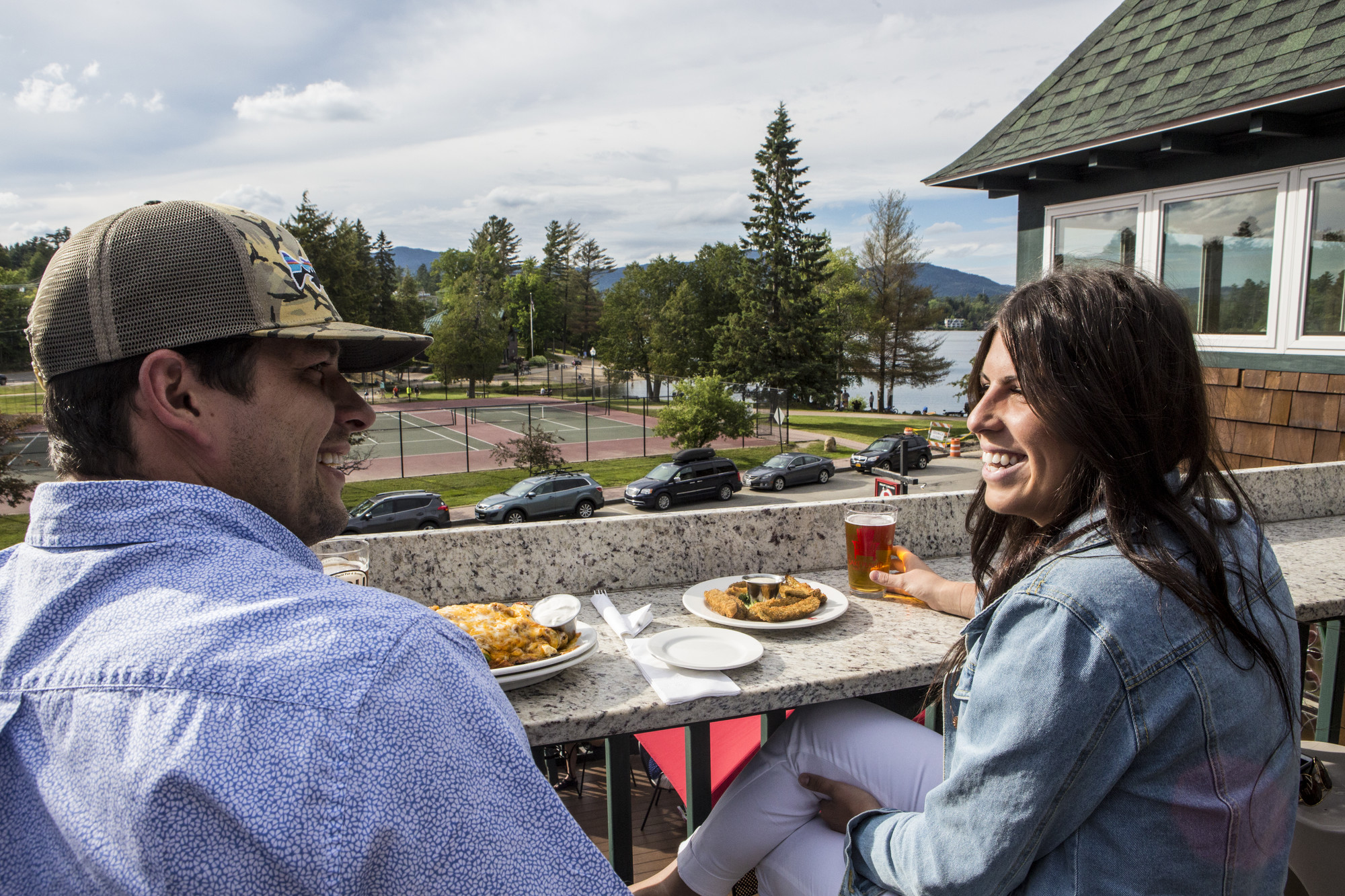A couple smiles as they enjoy a meal on an outdoor deck.