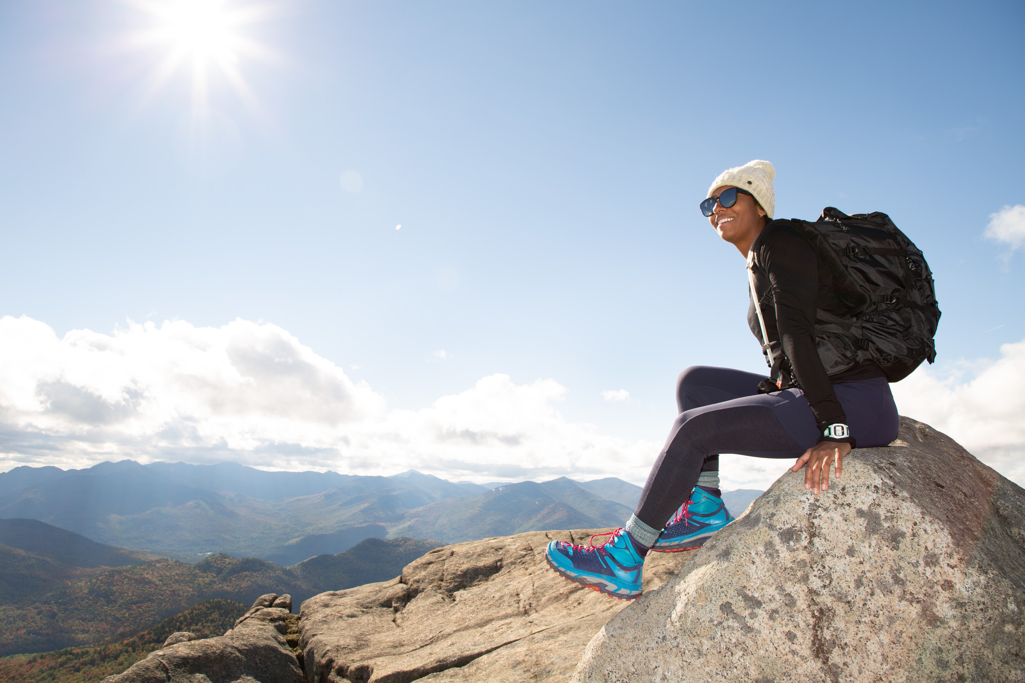 A woman sits on top of a rocky mountain&#44; overlooking the mountain range.
