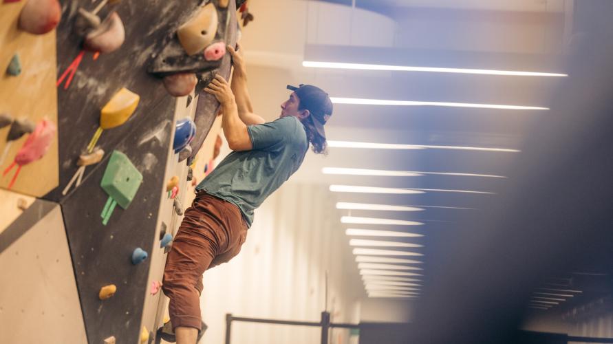 Man wearing backwards ball cap climbs bouldering wall in gym