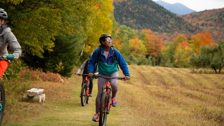 A woman bikes in an open field in fall.