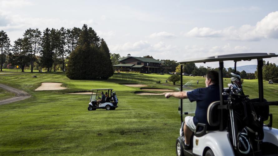 Two groups ride golf carts on a golf course.