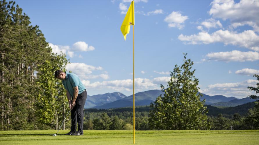 A male golfer tees up to a flag on the golf course.