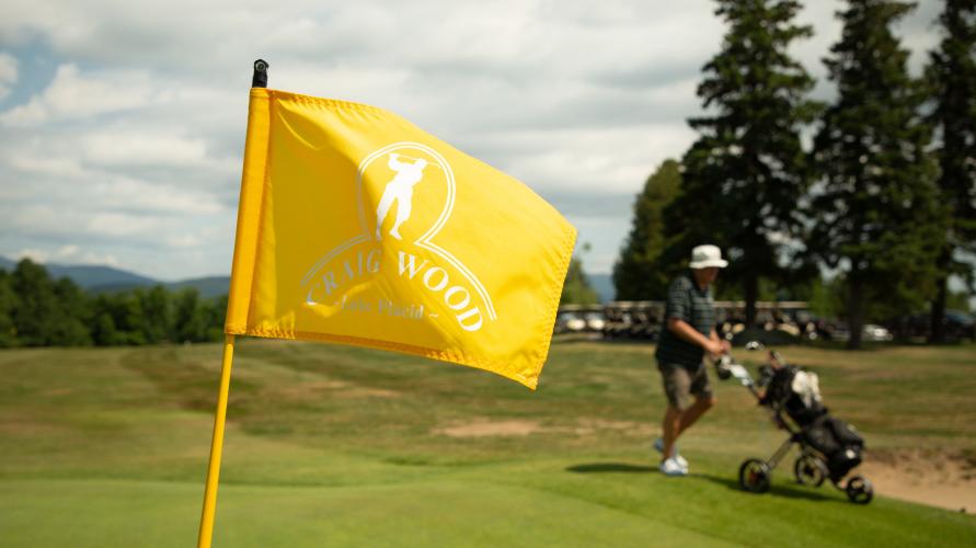 A golfer with cart passes behind the Craig Wood Golf Course flag.