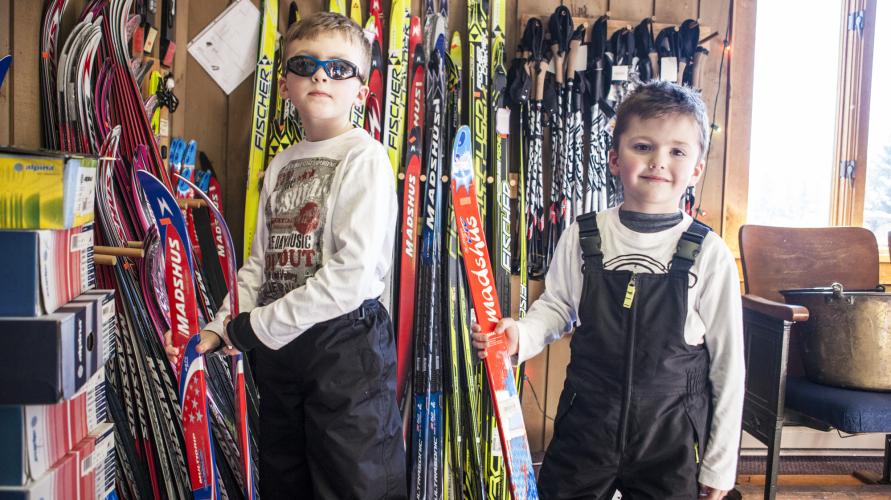 Two boys stand next to a ski rack inside Cascade Ski Center