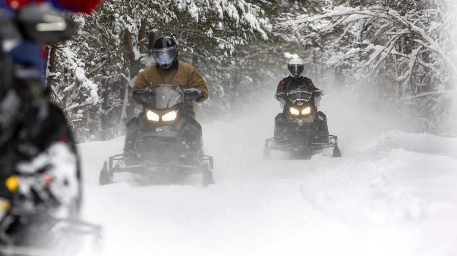Three snowmobilers riding on a groomed trail.