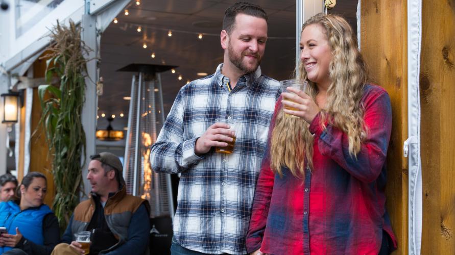 A man and woman in flannels stand drinking beer at fall event