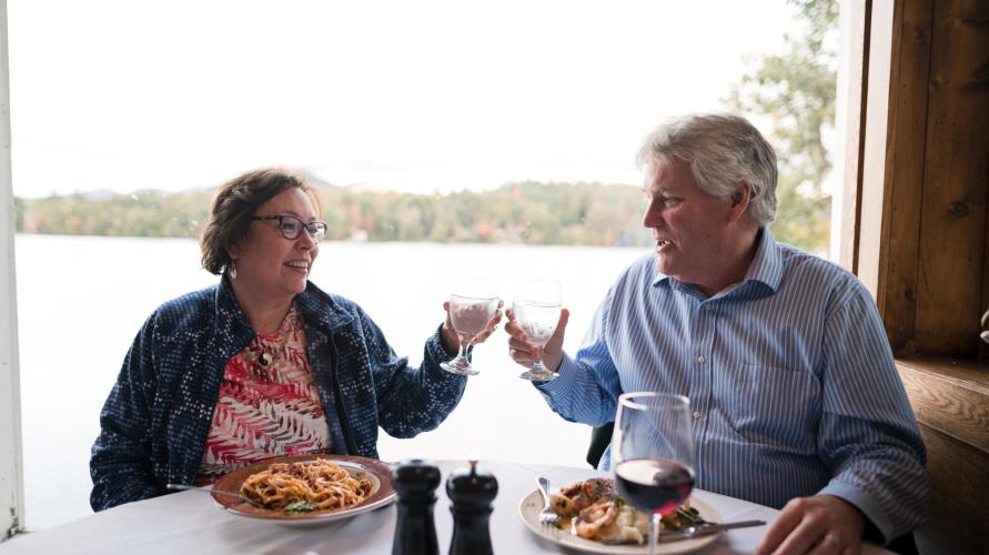 A middle-aged couple drink a toast at a lakeside restaurant in fall. 