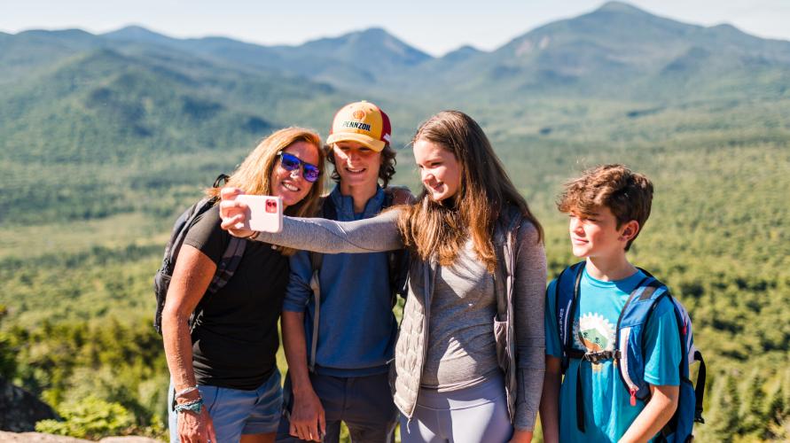 A family of four takes a selfie with mountains in the background
