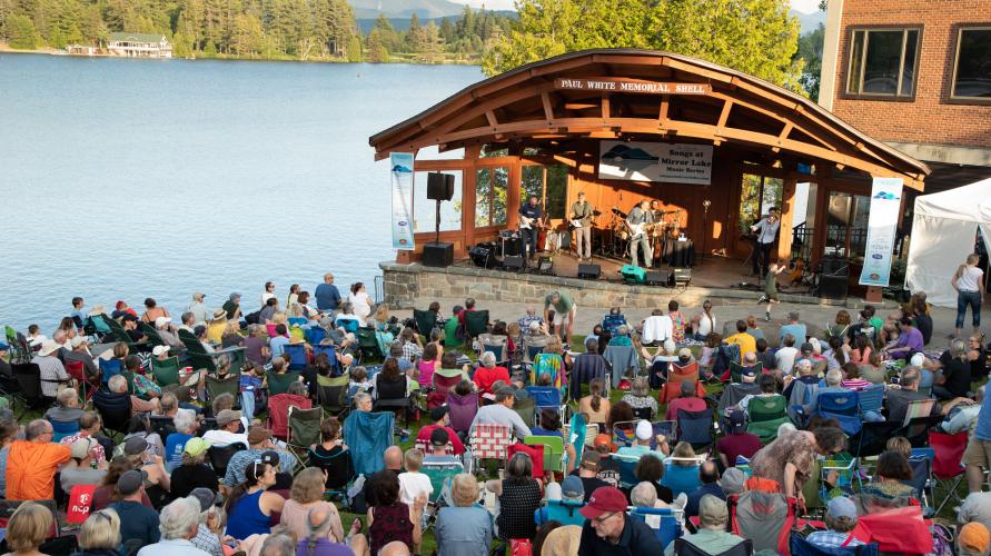 A large gathering of people at a bandshell by the water.